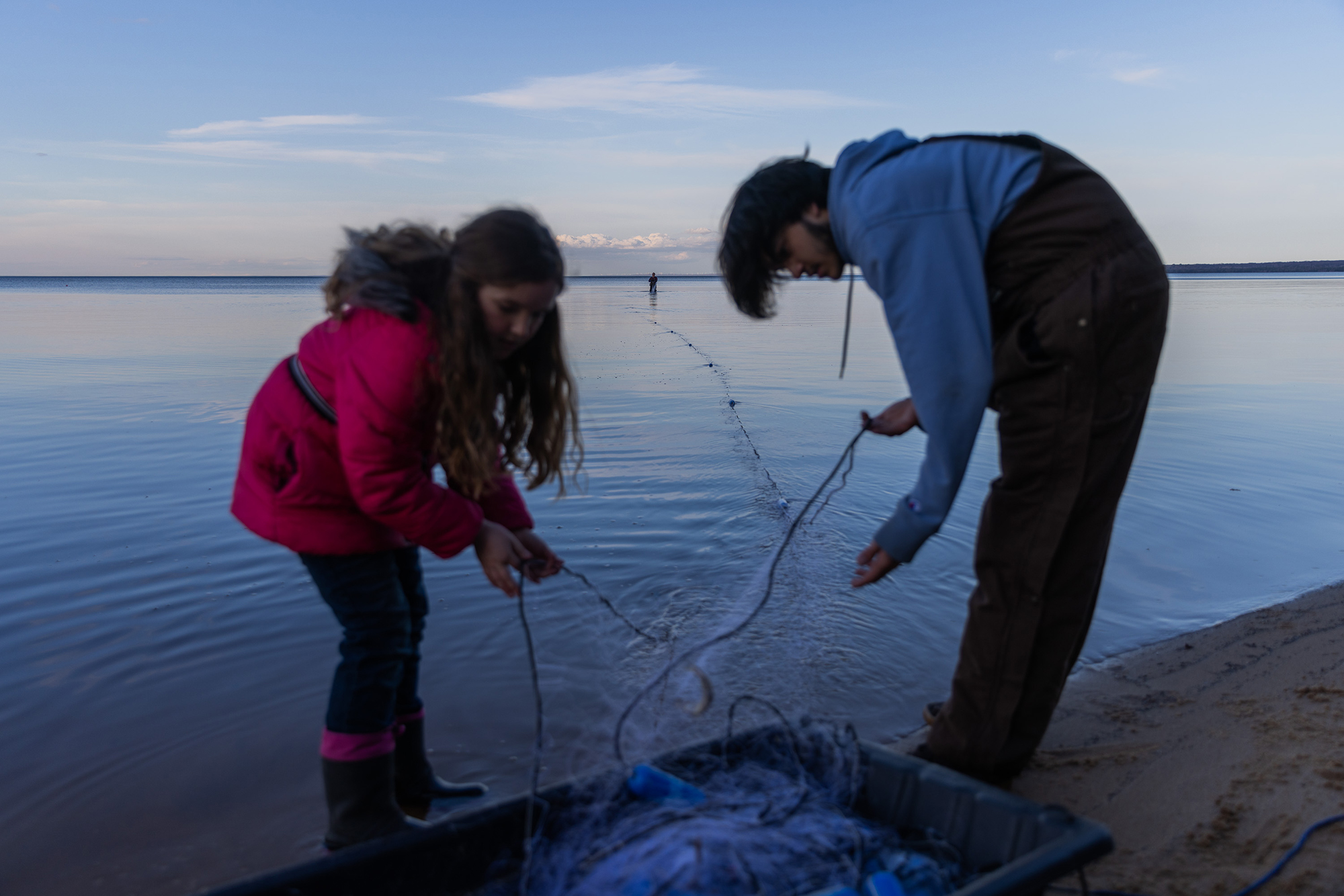 Two young people untangling a fishing net on the shore.