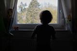 Child in their bedroom looking out their window.